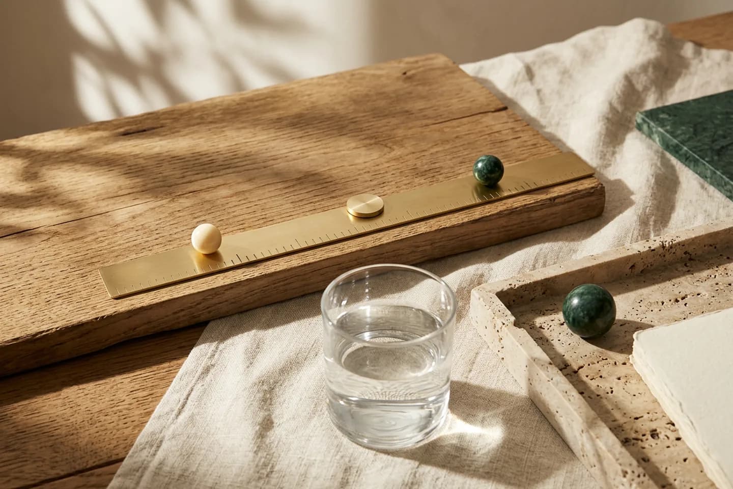 A plain brass ruler on an oak board with an ivory bead, a brass disc and a green marble sphere placed at three different points along it.